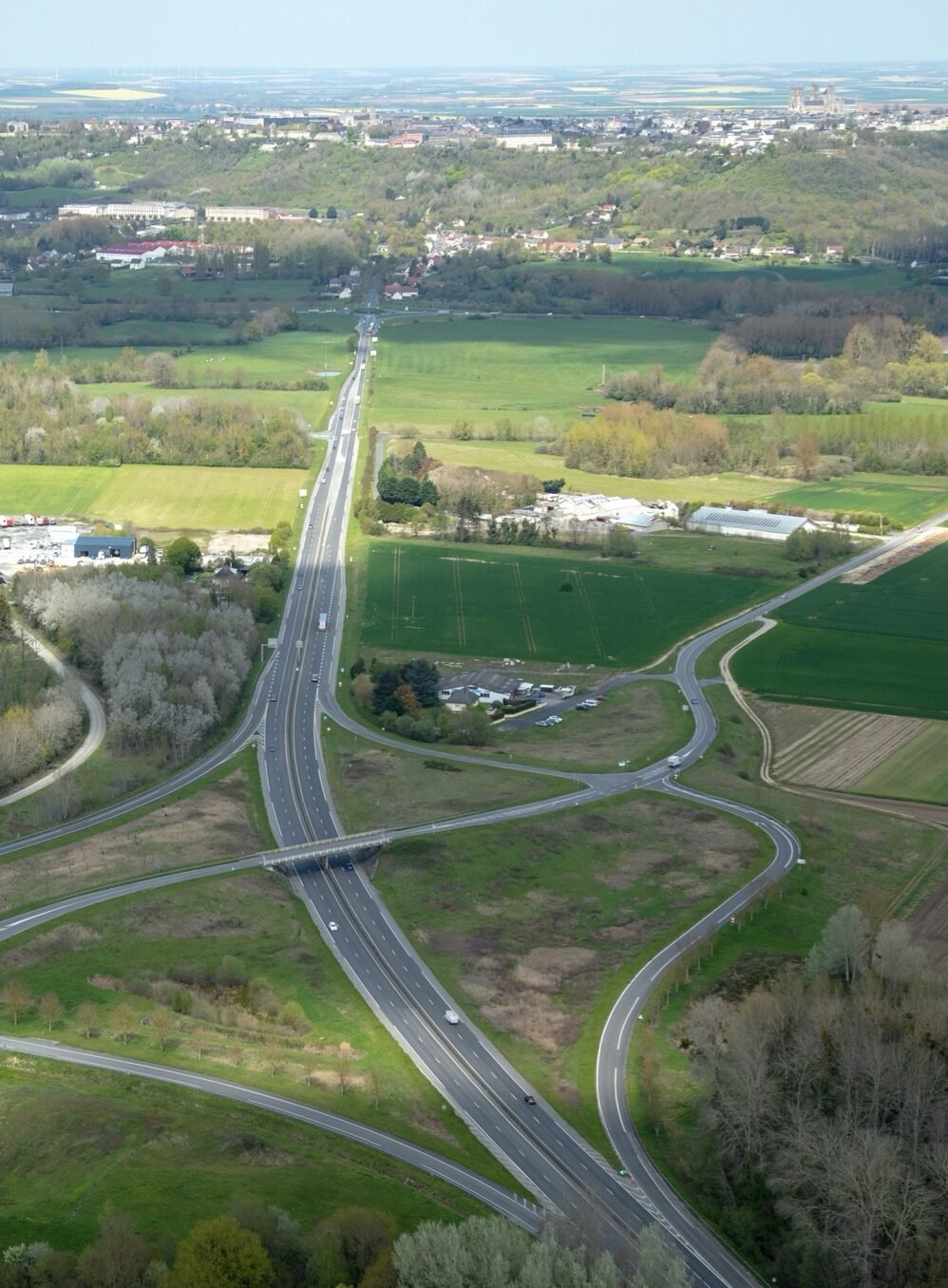 Vue aérienne de la RN2 traversant la plaine agricole au sud de Laon, avec les premières maisons de l’agglomération au premier plan.