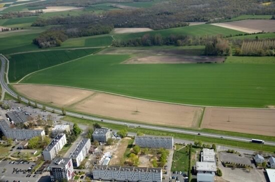 La RN2 à la hauteur du quartier Champagne, vue aérienne : la chaussée à deux voies longe des bâtiments d’activité et des champs.