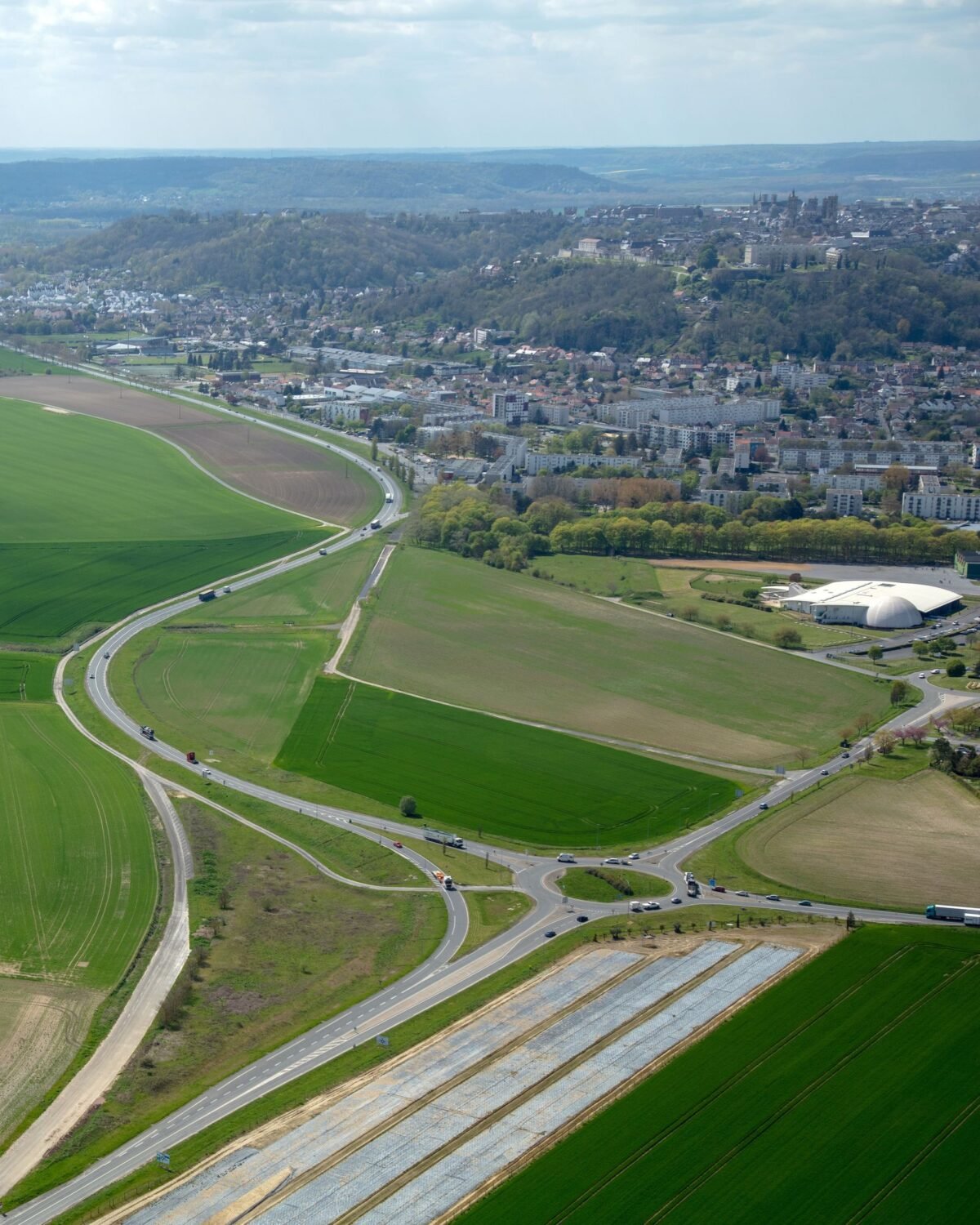 Vue aérienne du contournement de Laon : la RN2 à deux voies traverse la plaine agricole et rejoint l’agglomération ; la ville de Laon et sa cathédrale se détachent sur la butte, à l’horizon.